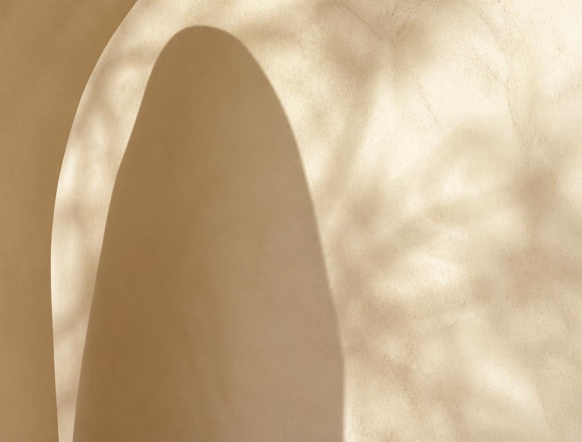 Arco de parede clara com sombra suave de folhagem
